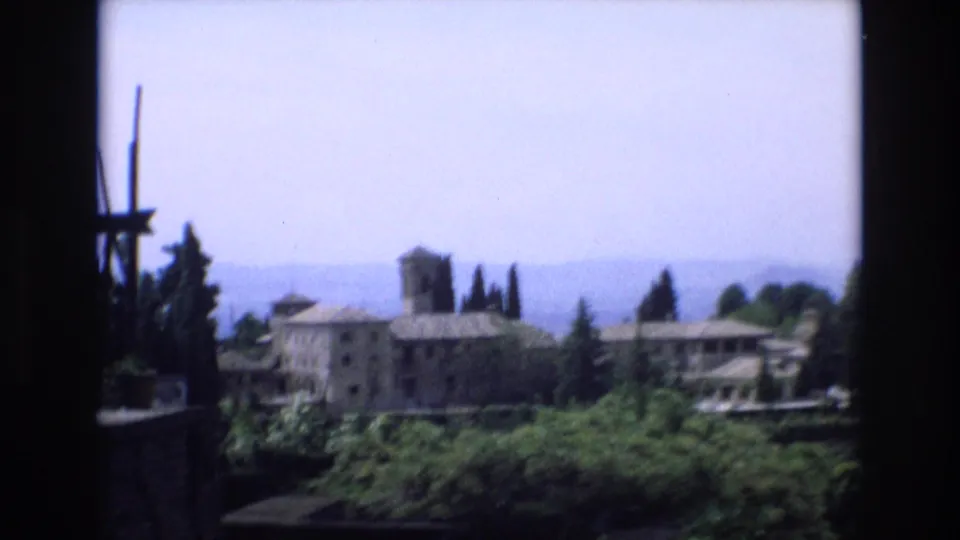 The final 8mm frame looks out from a shaded vantage point toward hillside buildings, trees, rooftops, and a hazy Spanish landscape.