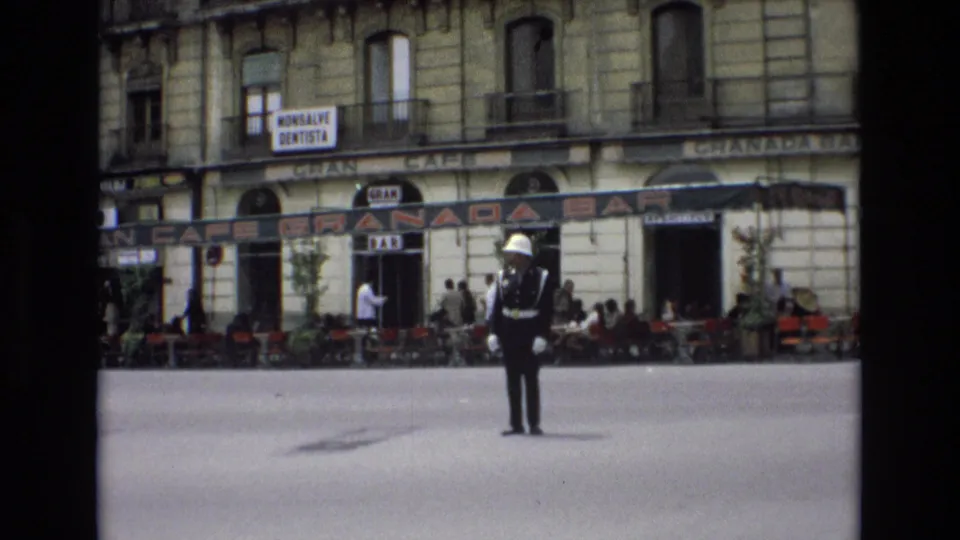 1972 Spain street scene with a white-gloved traffic officer standing at an intersection before Granada Bar signage, pedestrians, and outdoor seating.