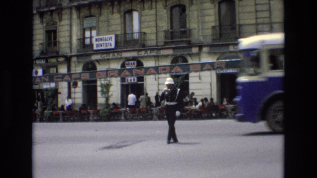 Traffic officer in the street as a blue-and-white bus enters the frame near storefronts.