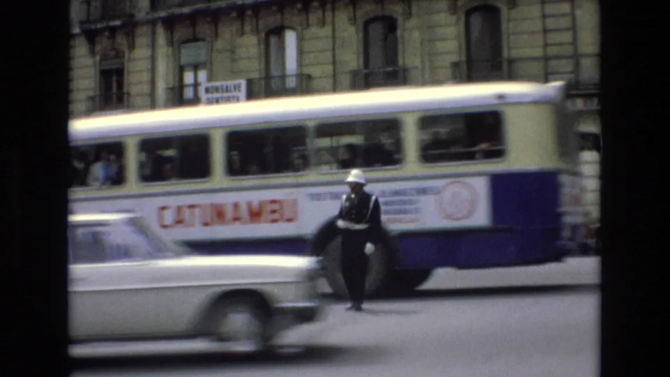 Traffic moves past a white-gloved officer as a blue-and-white bus and a blurred car cross the foreground in a 1972 Spanish city street scene.