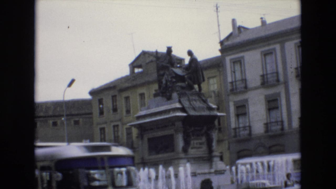 City bus passes in front of a monument and fountain in the square.