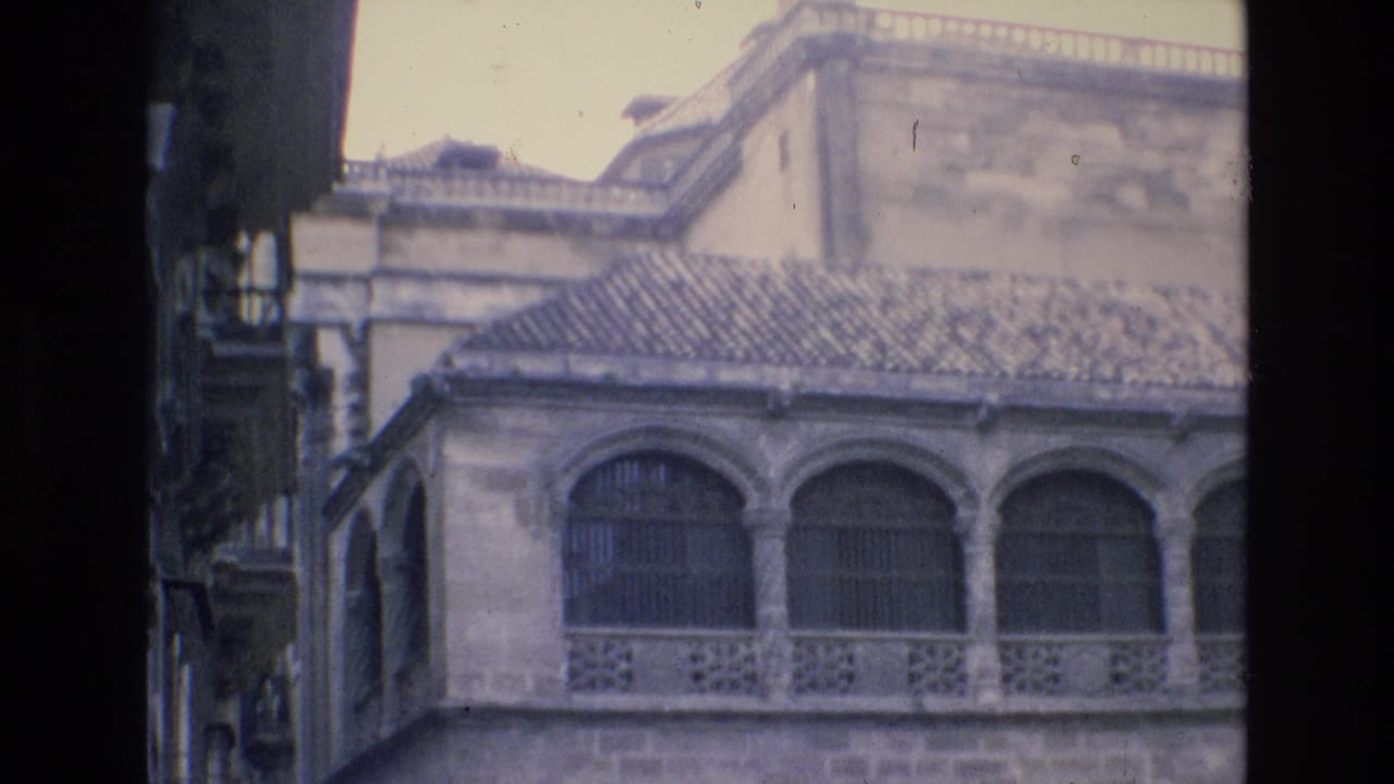 Upper portion of a stone building with arched windows, roof tiles and parapet detail.
