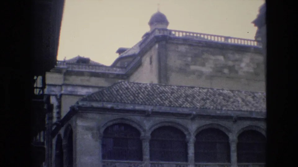 1972 Spain 8mm frame showing the building roofline, a small dome-like roof feature, stone parapet and lower arched openings from a handheld visitor viewpoint.
