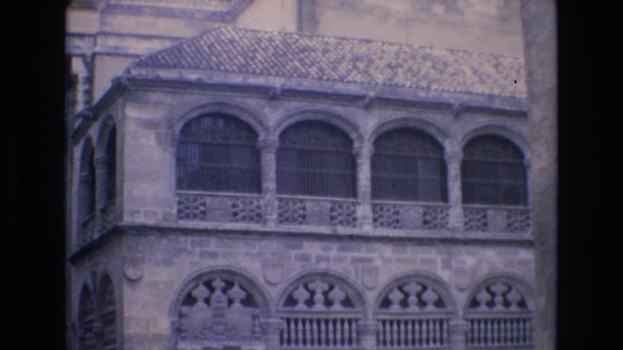 Stone building facade with rows of arched windows and decorative railing.