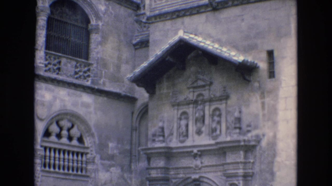 1972 Spain 8mm frame showing a historic stone facade with arched windows, iron grilles, carved balcony work, and a small tiled gable.
