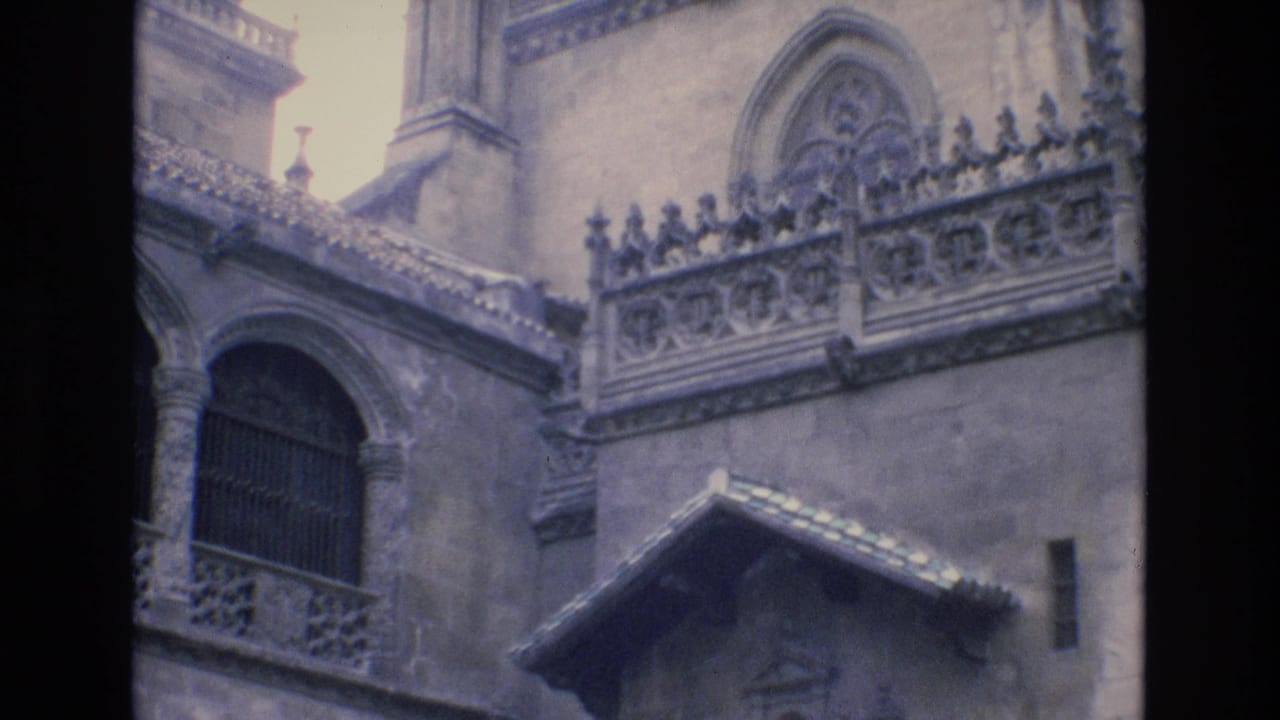 1972 Spain 8mm frame showing a historic Gothic-style stone facade with an arched barred window, ornate balustrade, and weathered roofline.