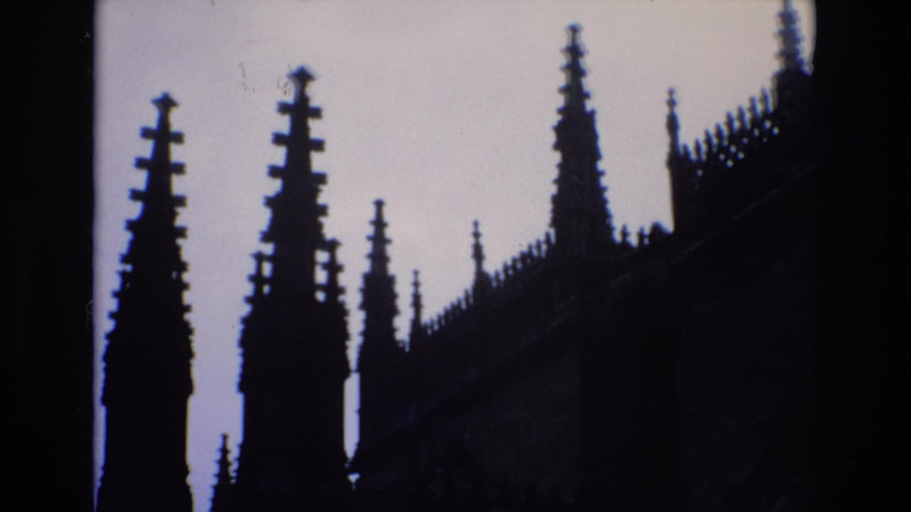 1972 Spain 8mm frame showing pointed Gothic spires and a crenellated roofline silhouetted against a pale sky, with the building mostly in shadow.