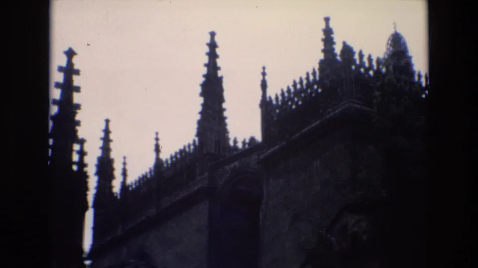 1972 Spain 8mm frame with multiple Gothic spires, roofline ornament, and a dark stone facade partly visible beneath a pale sky.