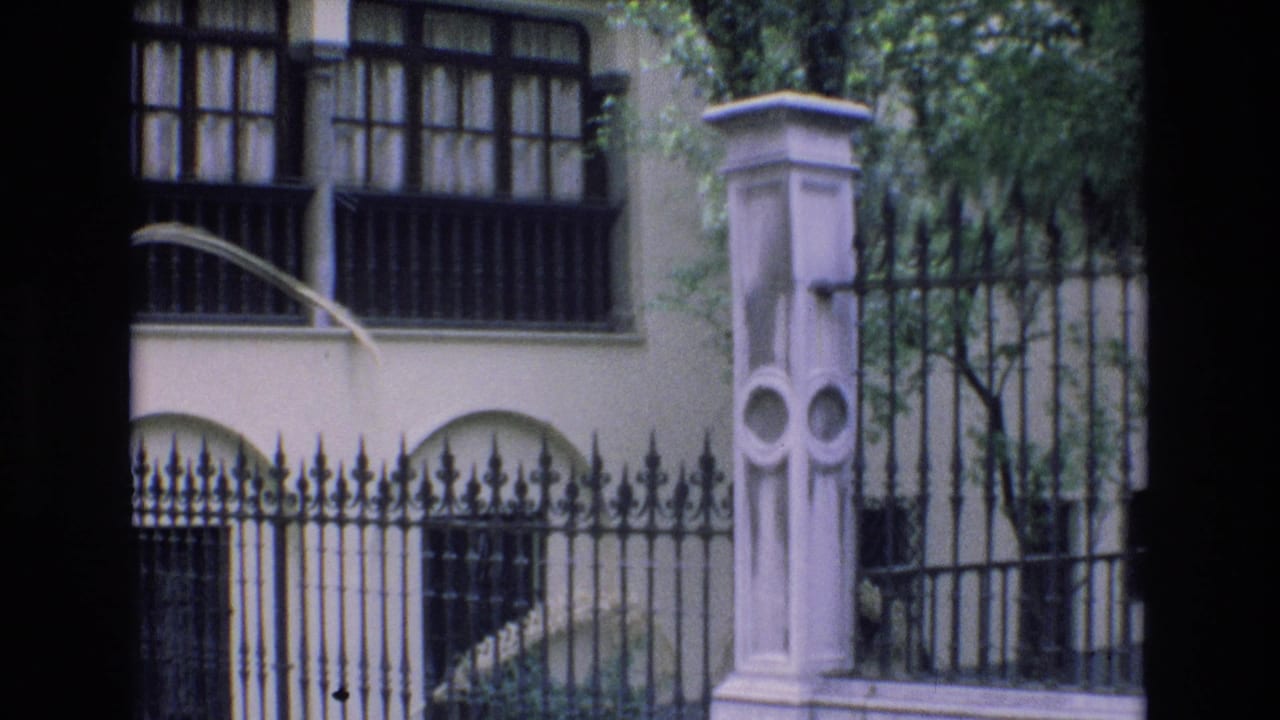 Iron fence and pale gate pillar in front of a cream building with barred windows.