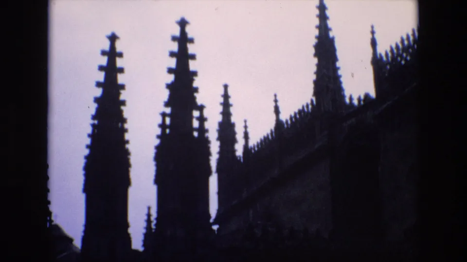 1972 Spain 8mm frame showing dark Gothic-style spires and roofline details silhouetted against a bright sky, with ironwork and building edges partly visible.