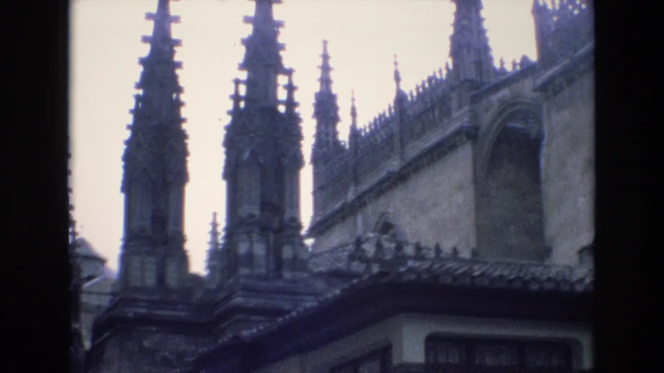 1972 Spain 8mm frame showing Gothic-style spires, a stone church-like exterior, a tiled roof in the foreground, and a partial cream building facade at the lower edge.