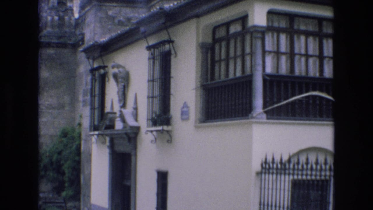 Similar building facade with enclosed balcony, barred windows, statue, and iron fence.