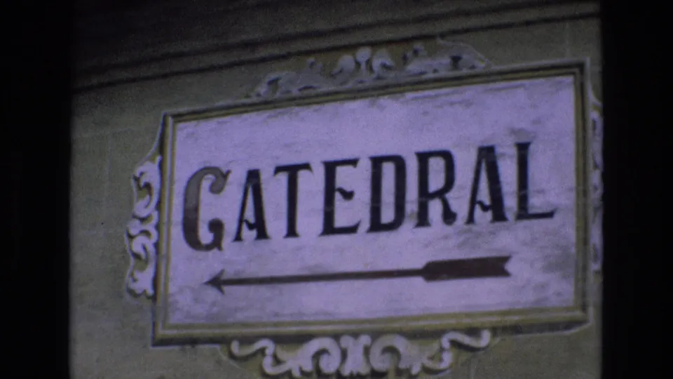 1972 Spain 8mm frame showing a weathered ornamental sign reading CATEDRAL with a left-pointing arrow on a wall.
