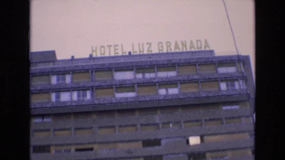 1972 Spain 8mm frame with an upward angled view of the HOTEL LUZ GRANADA sign and the hotel's concrete facade with repeated window bays.