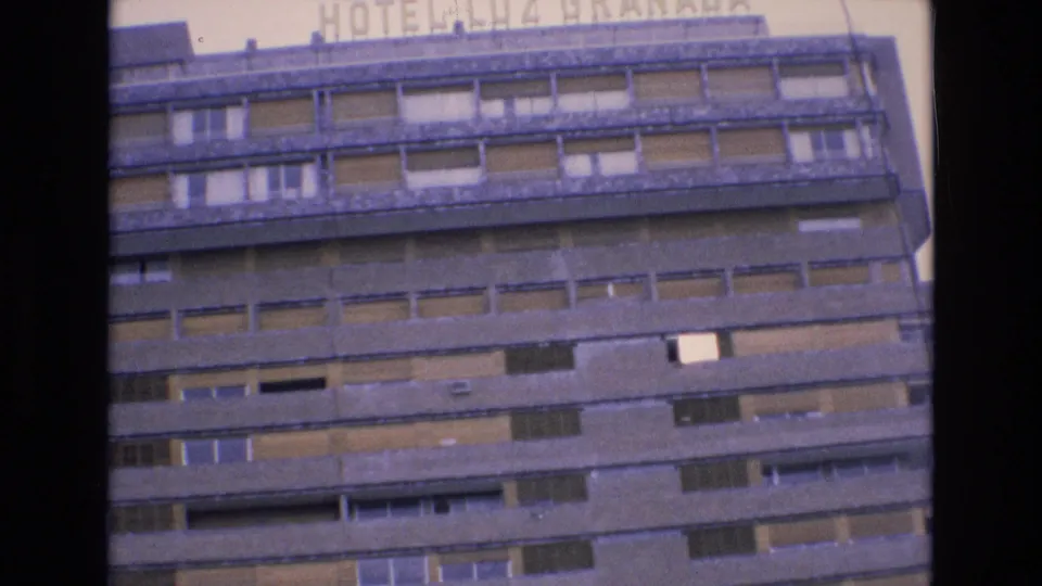 1972 Spain home-movie frame showing the upper stories of Hotel Luz Granada with repeated balconies, shuttered windows, and partial rooftop lettering.