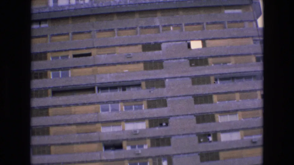 1972 Spain home-movie view of the hotel exterior continuing downward across stacked balcony bands, shuttered openings, and soft 8mm grain.
