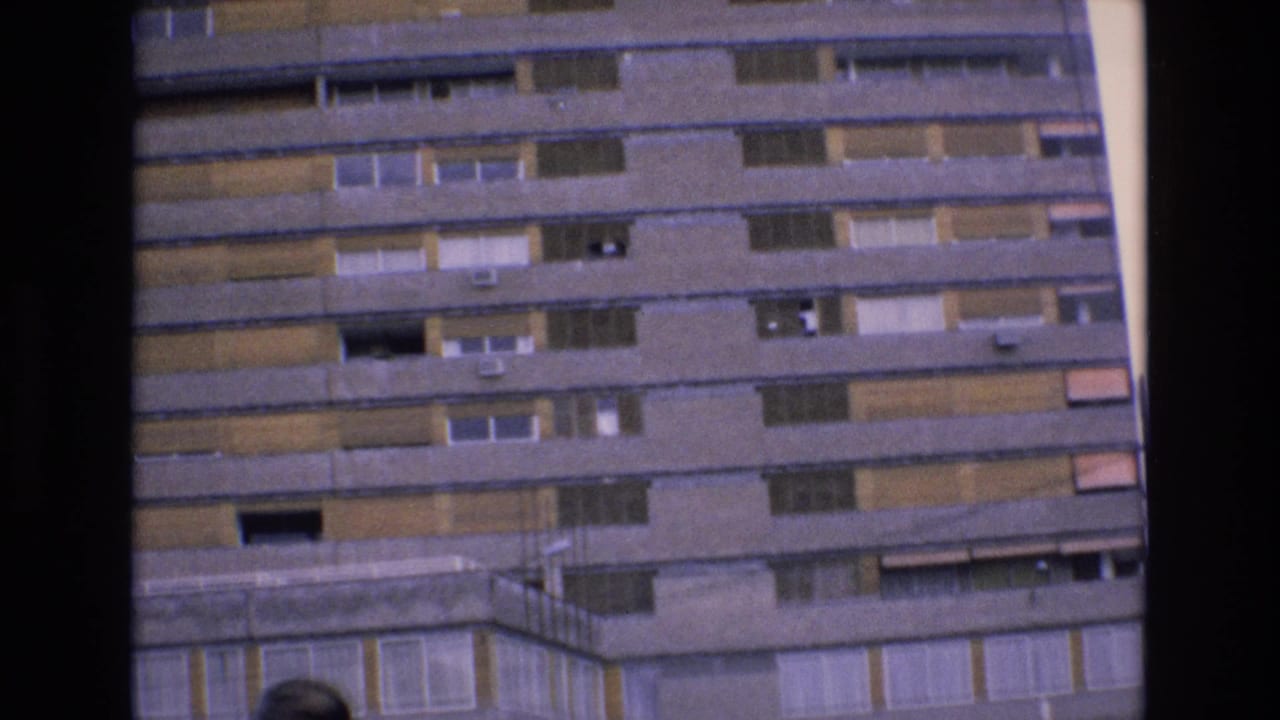 Upper stories of a large building with balconies, windows, and shaded openings.