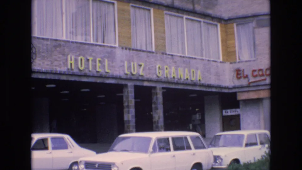 1972 Spain street-level hotel view showing Hotel Luz Granada signage, a shaded entrance, white parked cars, and partial El Cacil restaurant lettering at the right edge.