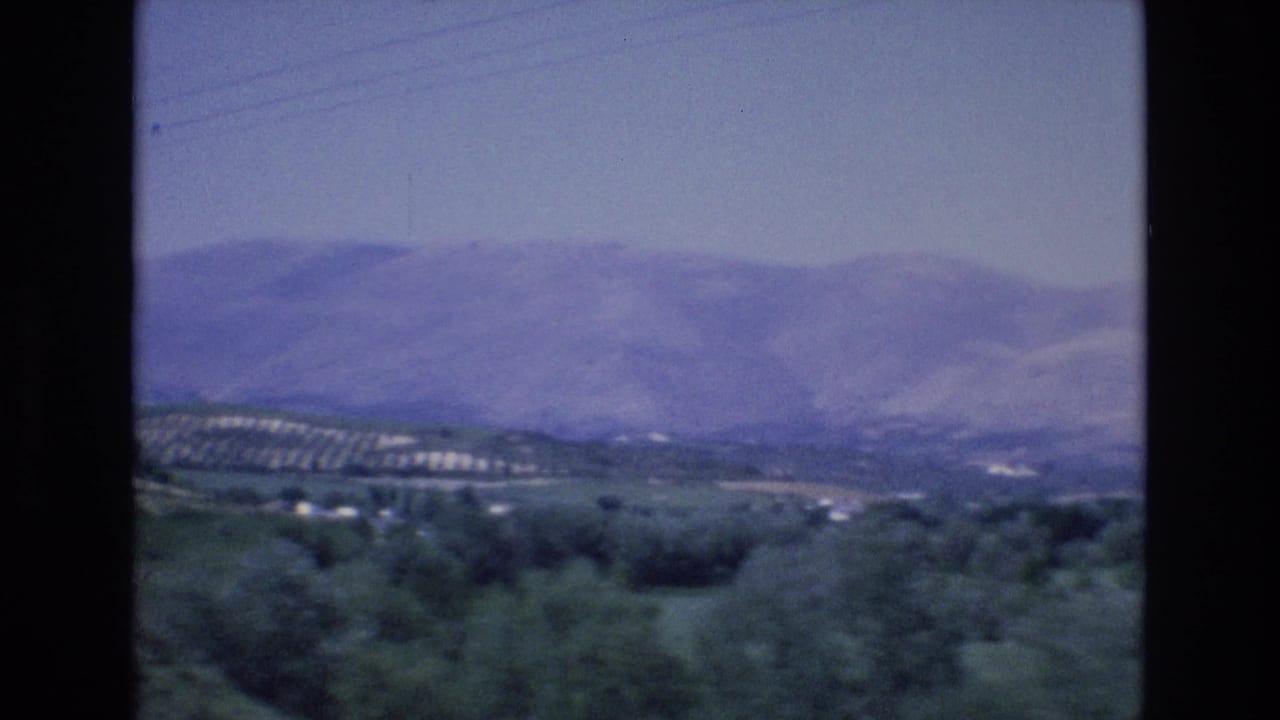 Distant mountain ridge above green countryside and cultivated hillside rows.