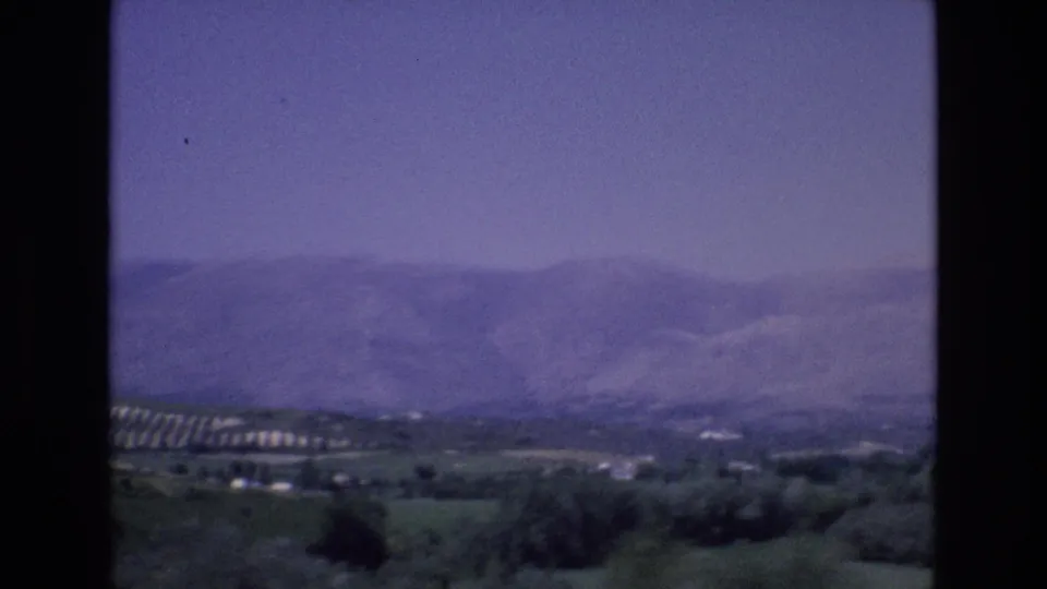 1972 Spain 8mm frame looking across a hazy mountain range and green valley from an elevated rural viewpoint.