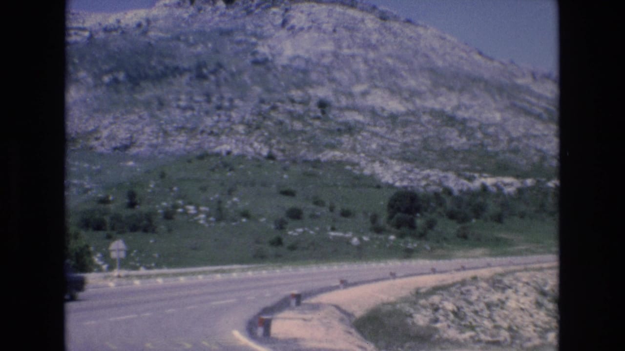 Curving paved road beside green slopes and a rocky hillside.