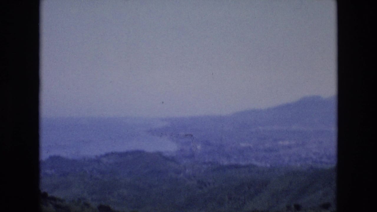 Distant coastline and hills seen through heavy haze with a small bright mark near the center.