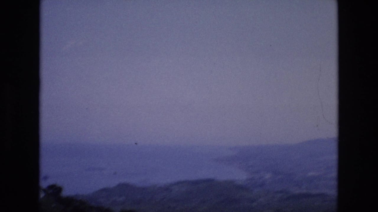 Distant coastline and ocean seen through a dark vertical film-frame edge.