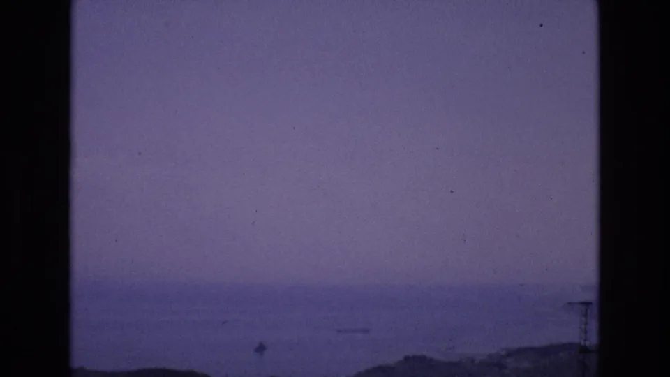 1972 Spain 8mm frame showing a distant calm sea, hazy purple-blue dusk sky, low shoreline, and dark scanned film edges.