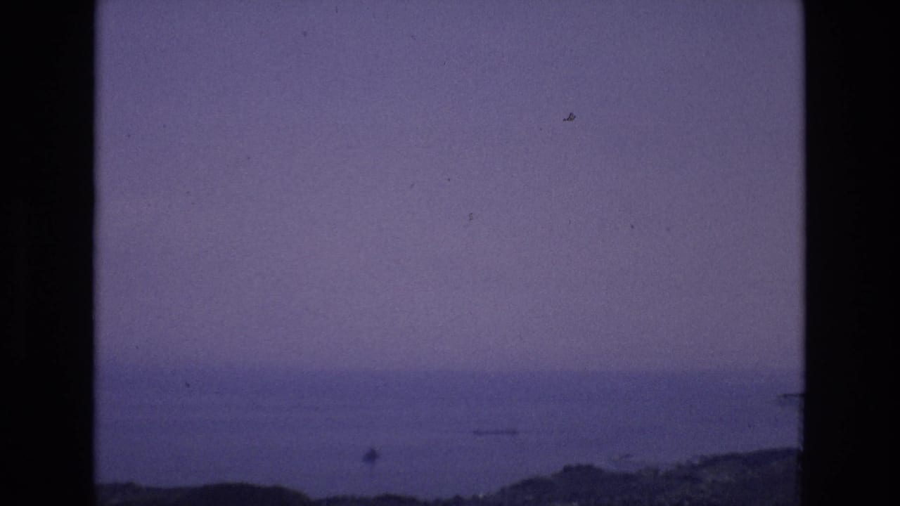 Spain 1972 8mm home-movie frame with a hazy distant water view, low shoreline or hills, film dust, and heavy black frame borders.