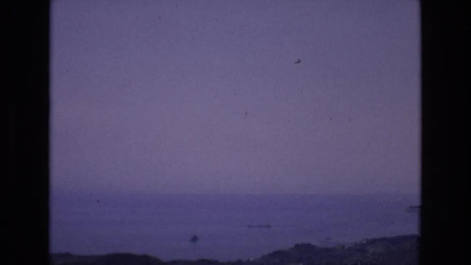 Spain 1972 8mm home-movie frame with a hazy distant water view, low shoreline or hills, film dust, and heavy black frame borders.