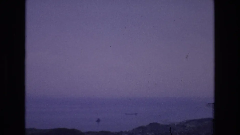Spain 1972 8mm frame showing a soft distant waterfront or bay scene with low hills, muted color, film specks, and strong black gate borders.