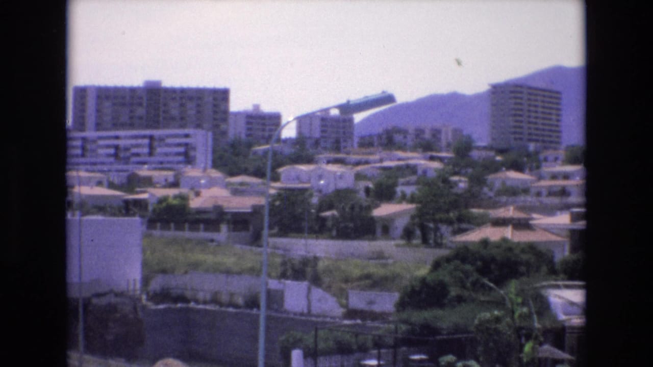 Similar cityscape view with apartment buildings, houses, trees, lamp poles, and mountains in the distance.