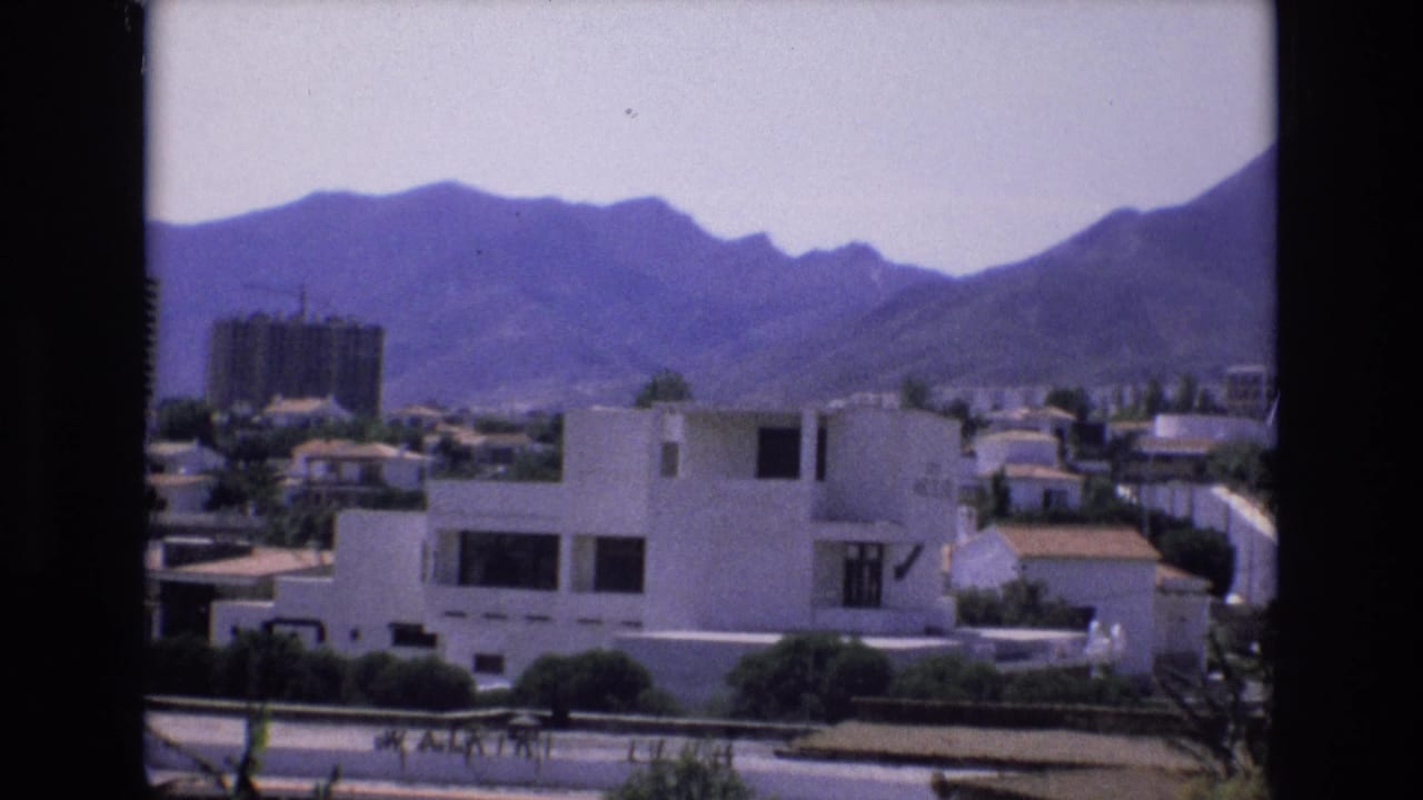 Suburban houses and a distant construction building beneath a mountain ridge.