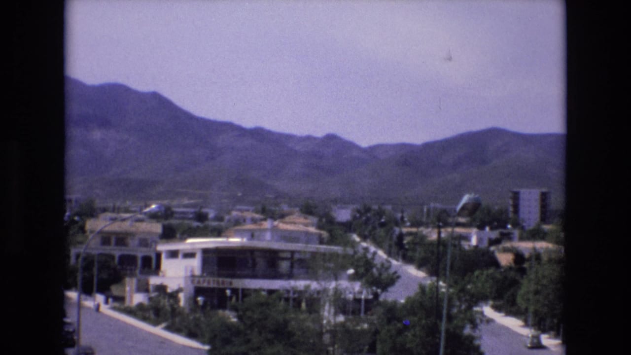Town street and cafeteria building below mountains, with trees and roadside structures visible.