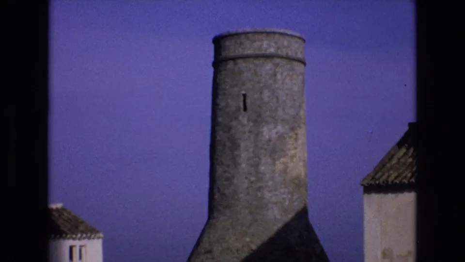 1972 Spain frame showing the cylindrical stone tower shifted slightly right, with a whitewashed structure and tiled roof visible along the edge.
