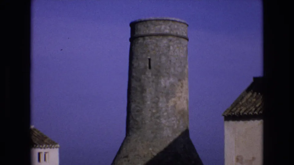 Final 1972 Spain frame showing the cylindrical stone tower held in a static composition between white buildings under a saturated purple sky.