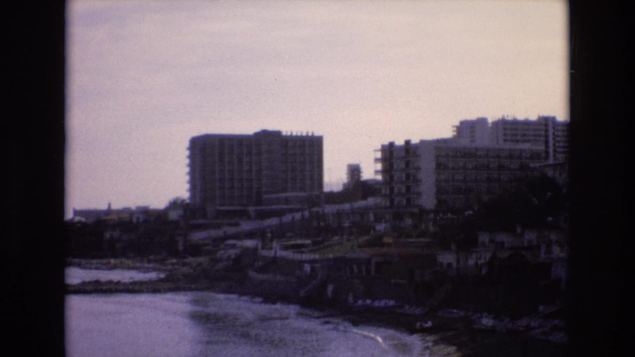 Large waterfront buildings overlook small waves along a rocky shore.