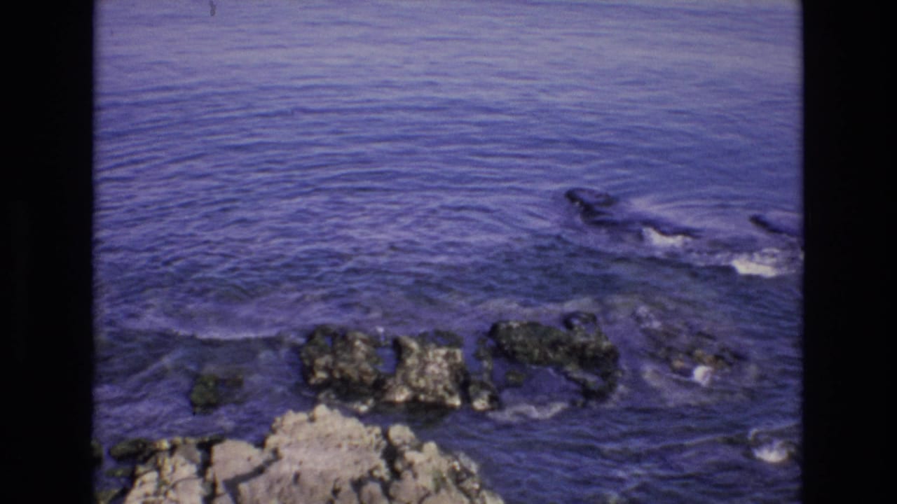 Current breaks into white foam as it moves past rocks along the shore.