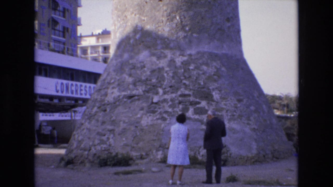 Couple viewed from behind as they look up at the rough stone base of a tower.