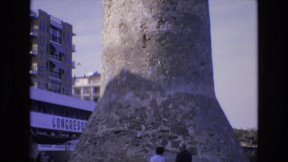 A wide 1972 Spain travel frame shows the weathered tower rising above two visitors near the bottom edge, with modern buildings and partial CONGRESOS lettering to the left.