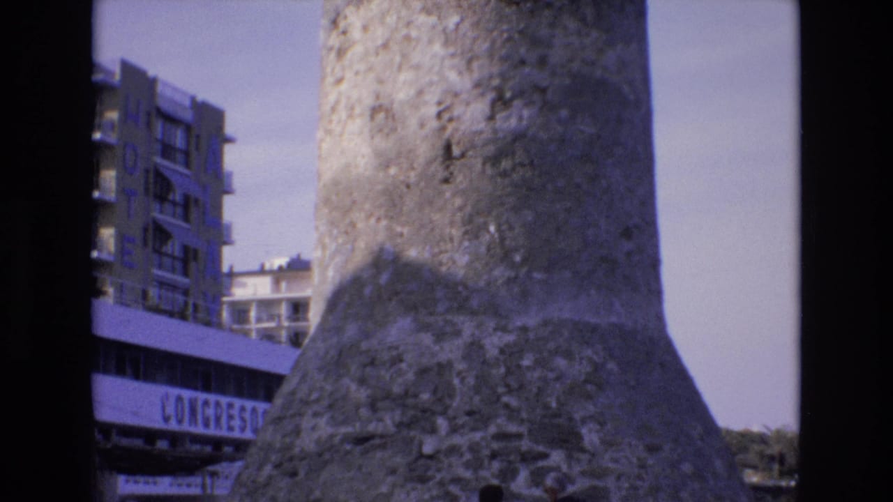 1972 Spain 8mm frame showing a weathered concrete tower in close view, with a multi-story hotel building and partial CONGRESOS signage in the background.