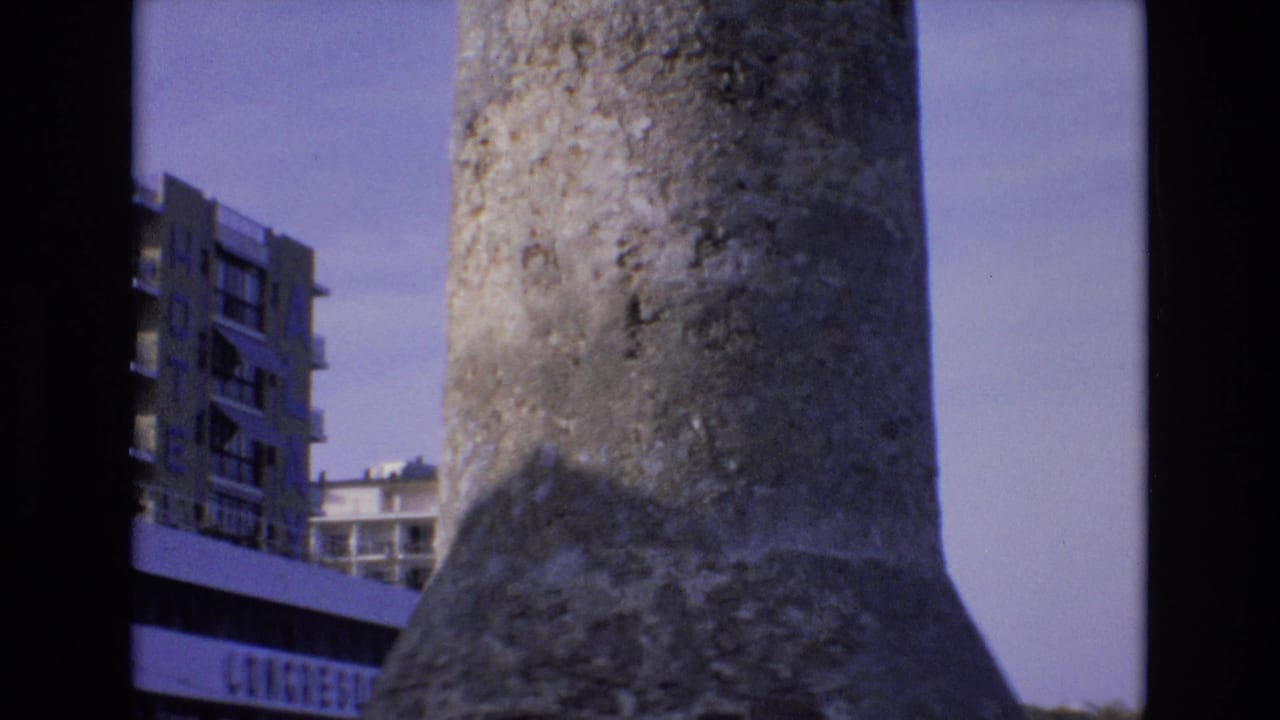 Concrete tower fills the foreground with a hotel building and partial signage in the background.