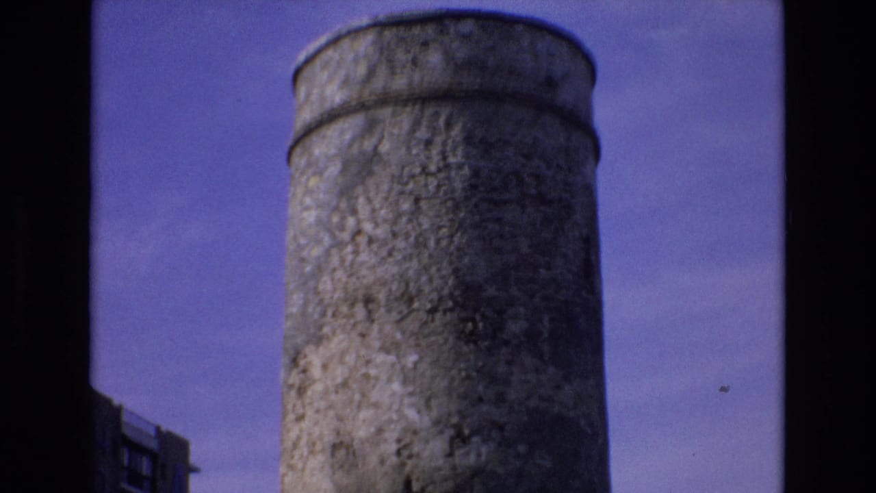 Cylindrical concrete tower rising against a blue-purple sky with a partial building edge at left.