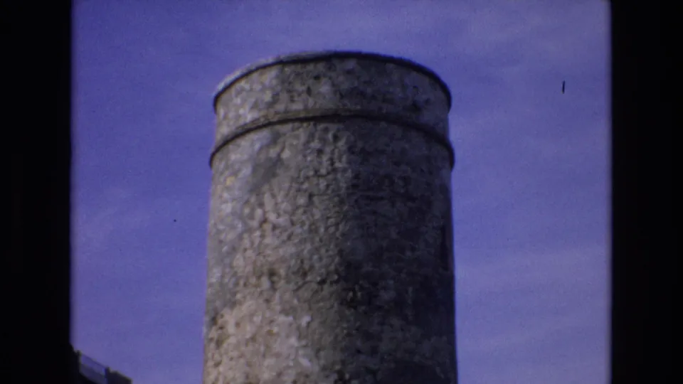 1972 Spain 8mm frame showing a closer low-angle view of the cylindrical tower, with textured concrete, rounded rim and visible film border at the left edge.