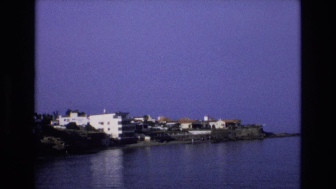 Coastal apartment buildings and houses viewed across blue water.