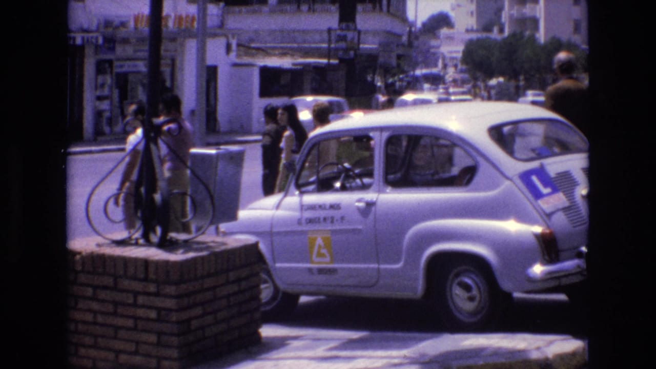 White learner car beside pedestrians on a bright city street.