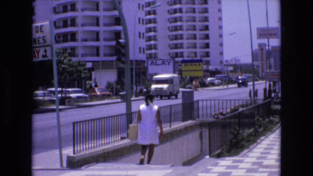 Woman in a white dress walking down steps beside a busy city street with cars, railings, tall buildings, and signs.