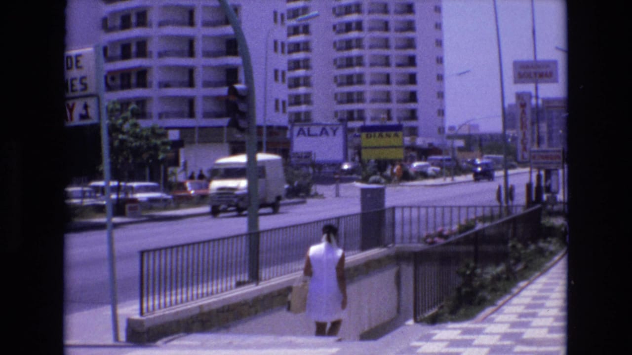 Woman descending steps near a railing as a white van and cars move along a city street lined with tall buildings and signs.