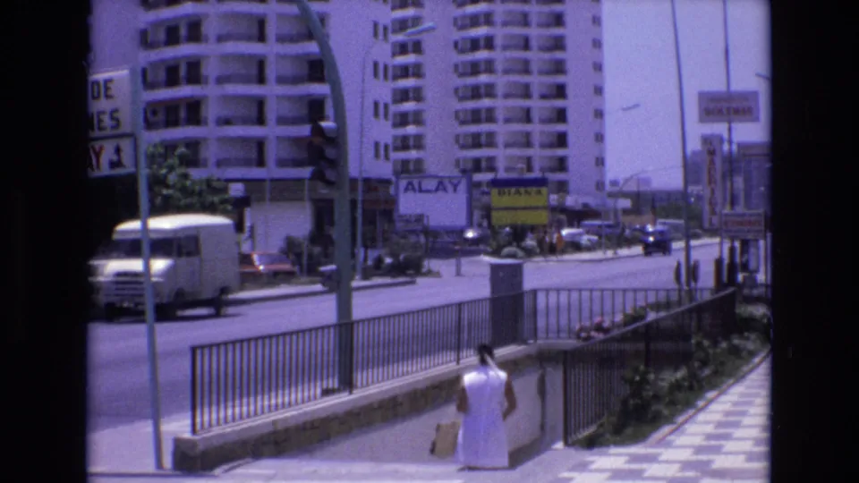 A white van moves through the foreground of the Spain 1972 urban street view as the woman continues descending the underpass steps beside railings and tiled pavement.