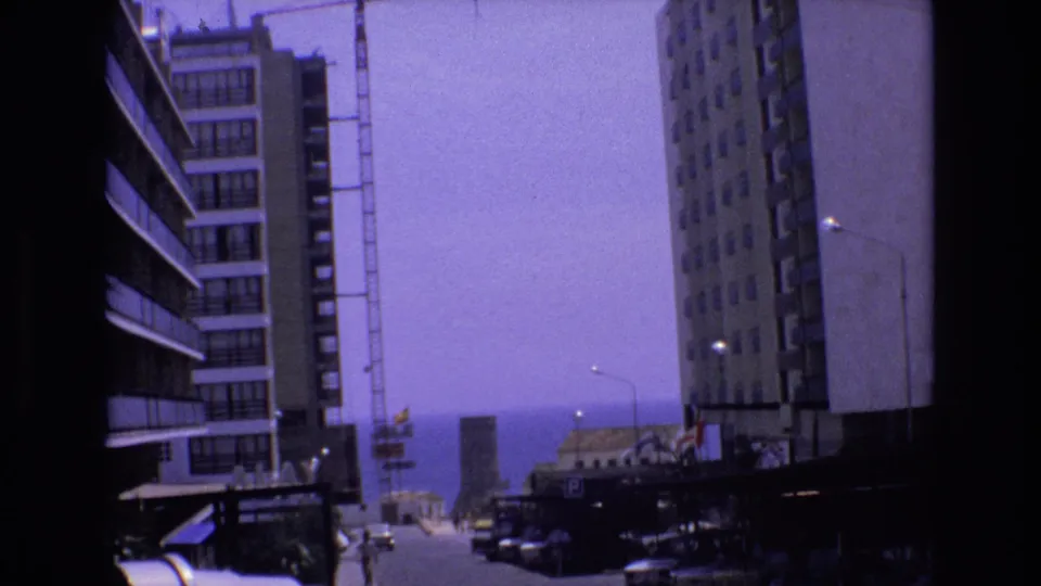 1972 Spain 8mm frame of high-rise buildings and a construction crane along a street leading visually toward the ocean.